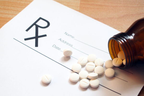 White tablets spilling out of brown glass bottle with blank Rx prescription form on wood table. Health care and medical concept. Selective focus.